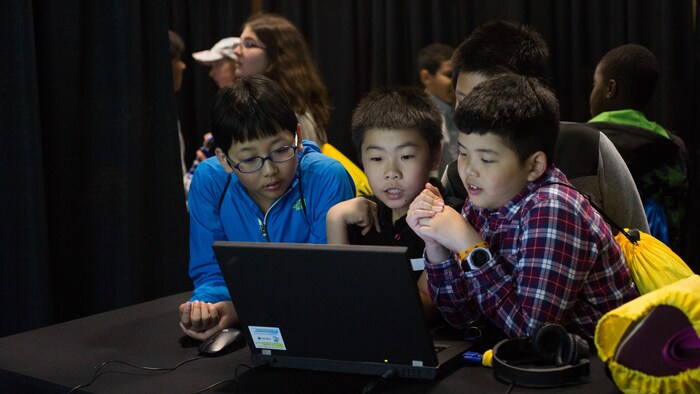Trois garçons regardent avec attention un ordinateur dans une pièce sombre. 