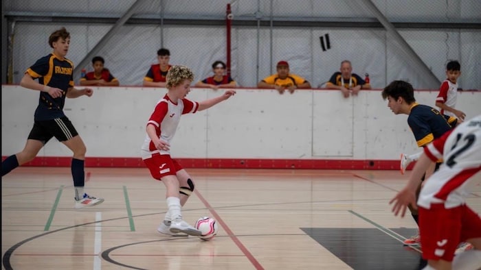 Un jeune joueur de futsal manie le ballon devant un défenseur durant un match.