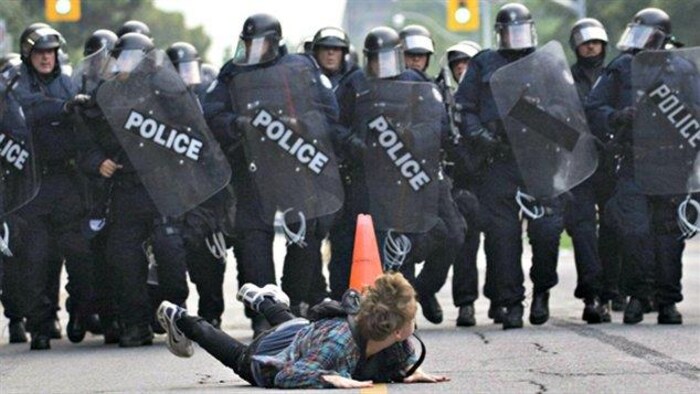 Le protestataire est couché sur le ventre, avec derrière lui un mur de policiers en marche.