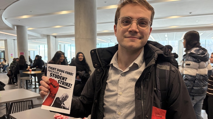 L'étudiant porte un carré rouge et tient un dépliant encourageant les étudiants à faire la grève.