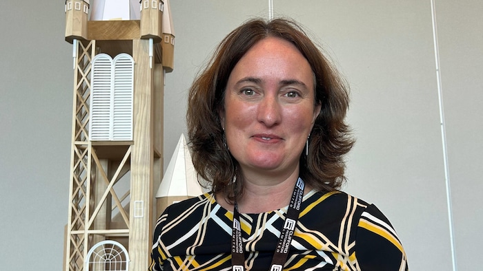 Gabrielle Bardall pose pour une photo, devant une maquette d'une église en bois.