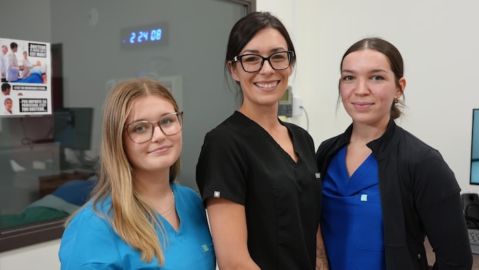 L'enseignante en soins infirmiers est entourée de deux étudiantes, les trois femmes regardent l'objectif.