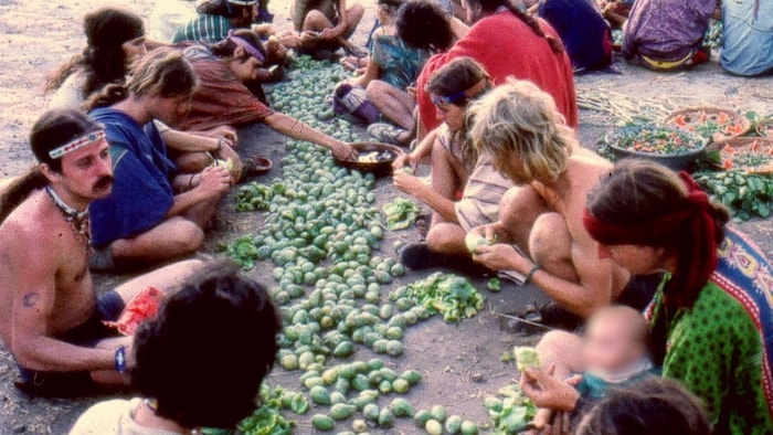 On voit des jeunes personnes assises par terre, en train de préparer des légumes.