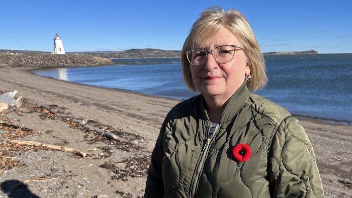 Une femme sourit à la caméra, la mer derrière elle.