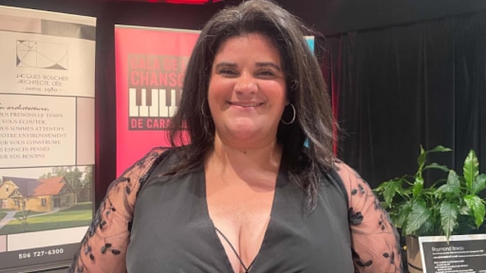 Une femme souriante devant la bannière du Gala de la chanson de Caraquet. 