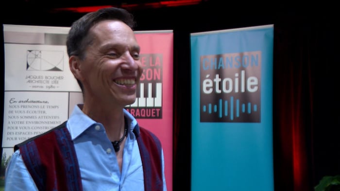 Un homme souriant devant une bannière du Gala de la chanson de Caraquet. 