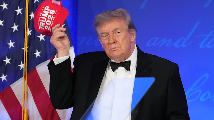 Donald Trump tient une casquette rouge dans sa main.