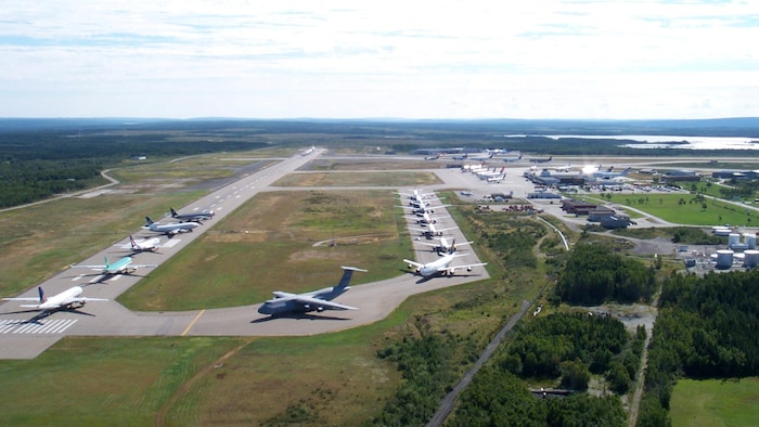 Photo aérienne d'une douzaine d'avions posés en rang sur la piste d'atterrissage d'un aéroport.