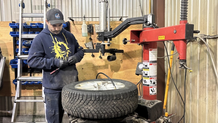 Un mécanicien travaillant avec des gants prépare une roue installée sur une machine de montage et d'équilibrage de pneus dans un garage.