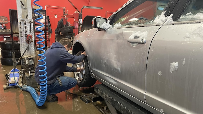 Un garagiste installe un pneu sur une voiture enneigée.