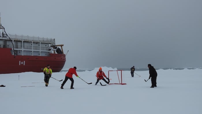 Cinq personnes jouent au hockey devant le navire de la Garde côtière canadienne, en Arctique.