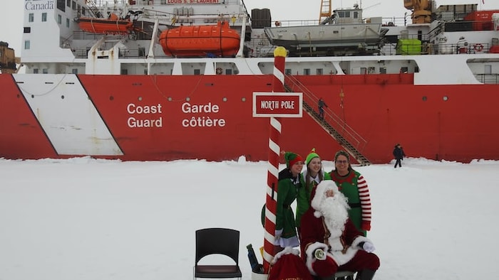 Trois membres de l'équipage sont déguisés en lutins et sourient aux côtés du père Noël, devant un navire de la Garde côtière canadienne.