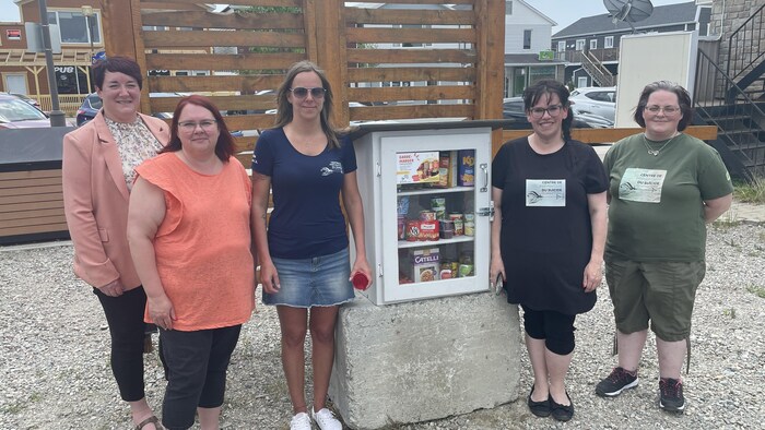 Cinq femmes posent à l'extérieur, autour d'un petit garde-manger communautaire.