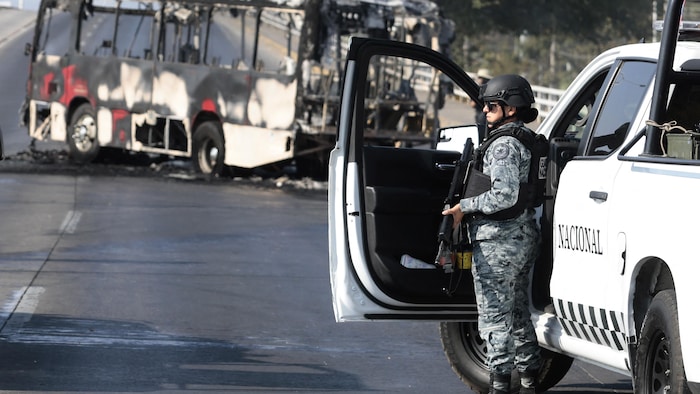 Un membre de la Garde nationale armé se tient à côté d'un camion, près d'un autobus incendié.