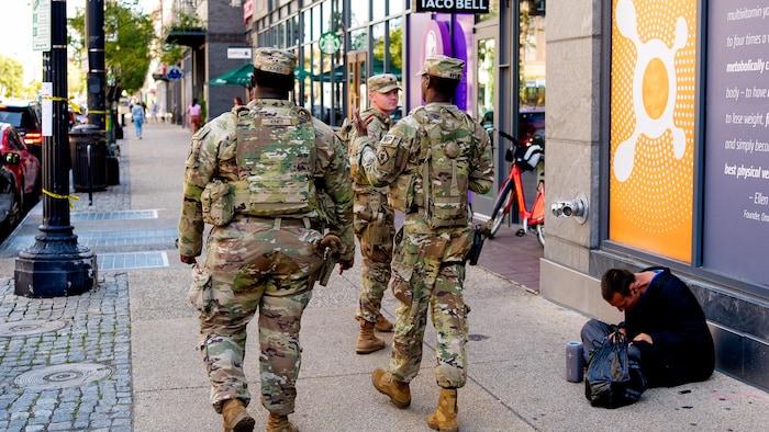 Des militaires de la Garde nationale en patrouille dans une rue de Washington passent devant un itinérant, le 29 août 2025.