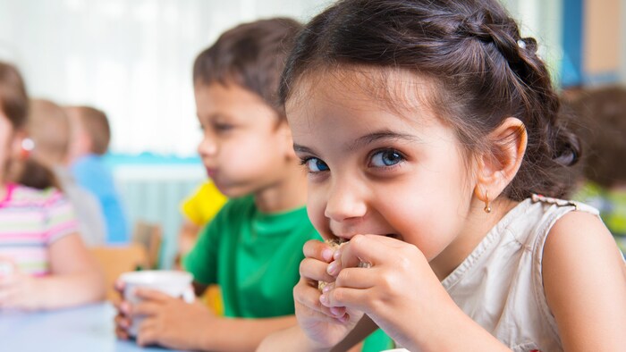 Une petite fille croque dans un biscuit à la garderie et regarde la caméra.