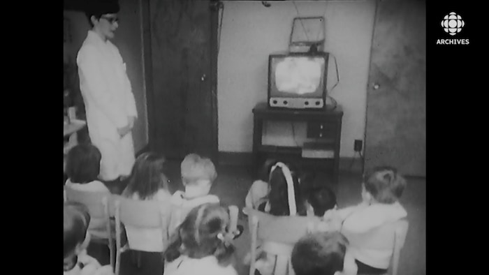 Un groupe d'enfants assis devant la télévision sous la supervision d'une éducatrice.