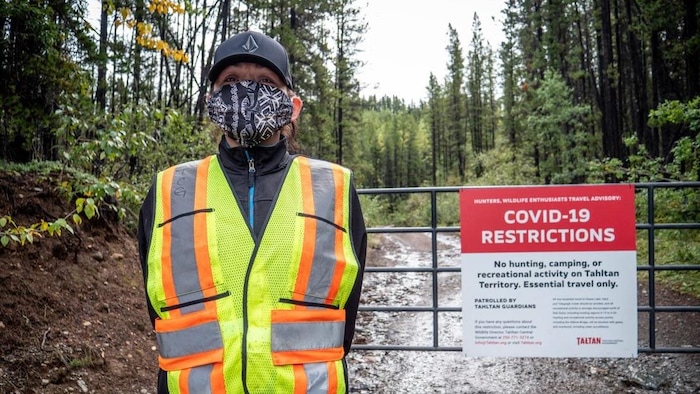 Una mujer con máscara vigila una valla en la que un cartel pide a los cazadores y a los amantes de la naturaleza que no pasen a causa del COVID-19.