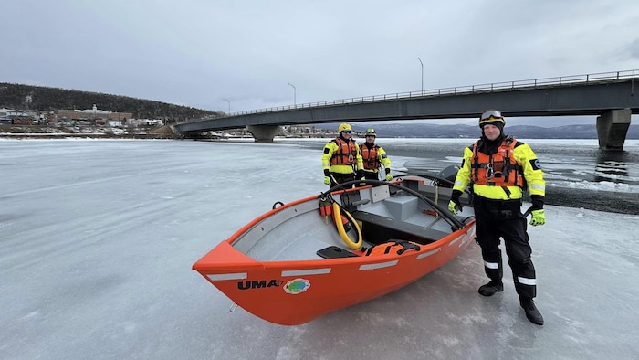 Trois pompiers autour d'un bateau sur la glace dans la baie de Gaspé.