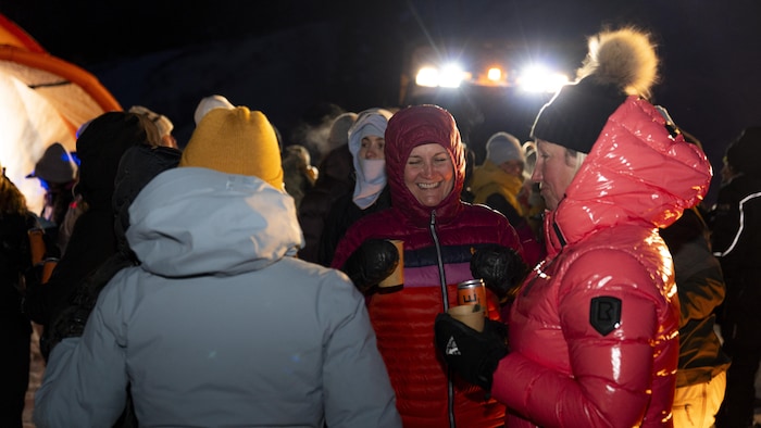 Plusieurs femmes en tenue d'hiver sont regroupées de nuit, en extérieur.