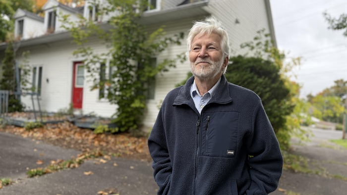 Gaston Cadrin devant une maison canadienne regarde au loin.
