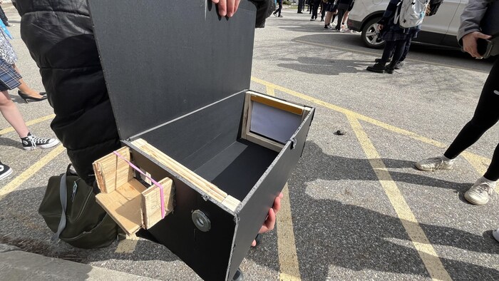 Un évèle montre sa boîte préparée pour l'éclipse, le 8 avril, dans le stationnement du Collège Nouvelles Frontières. 