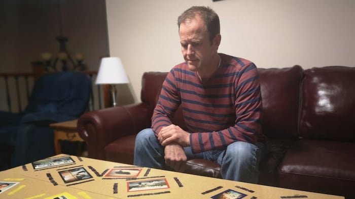 Cory Baylis regarde des photos de famille éparpillées sur une table.