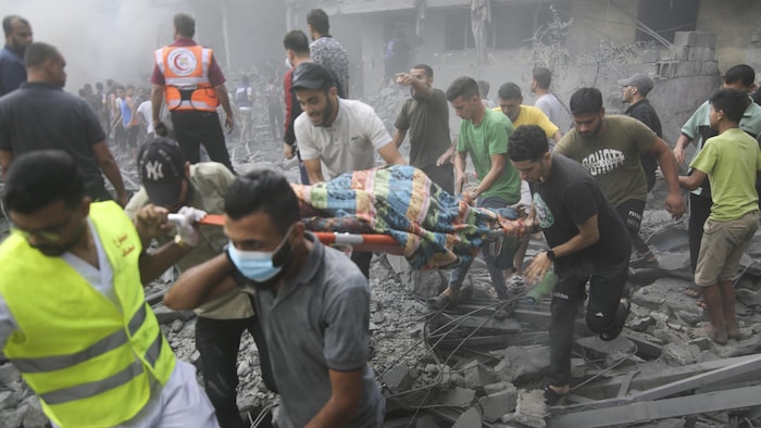 Des Palestiniens évacuent un blessé sur une civière, au milieu de gravats.