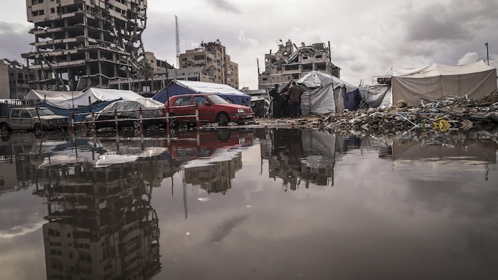 Une immense mare d'eau, des tentes et des amas de gravats près d'immeubles en partie détruits par des frappes.