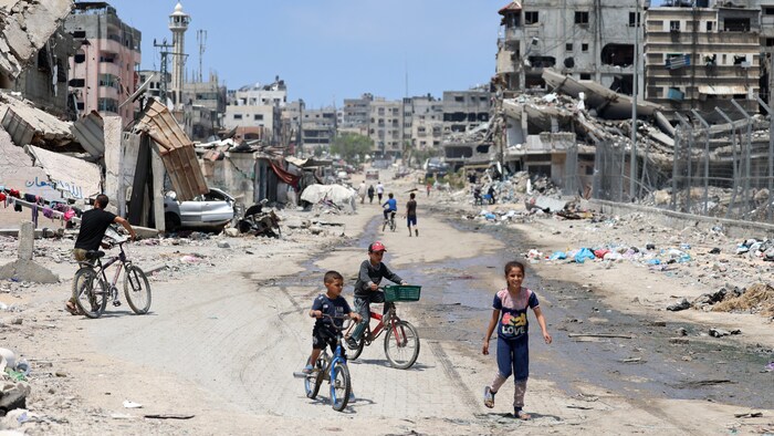 Des enfants font du vélo dans une rue dévastée par les bombardements.