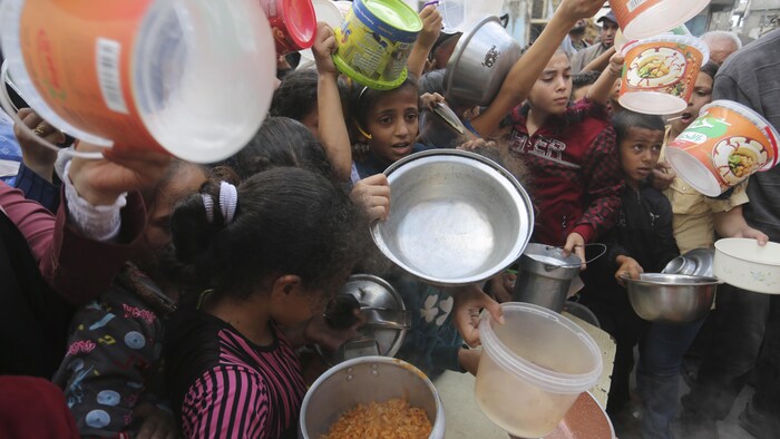 Des enfants palestiniens tendent leurs bols à la recherche de nourriture. 