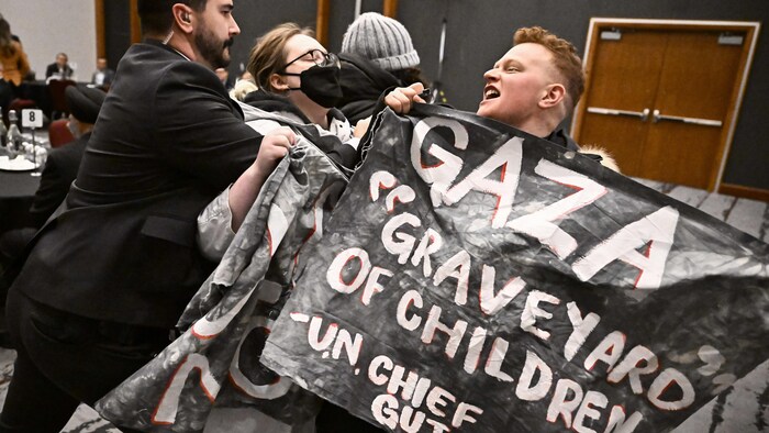 Un agent de la GRC repousse des manifestants, dont un qui tient une pancarte en anglais sur laquelle on peut lire «Gaza, cimetière d'enfants».