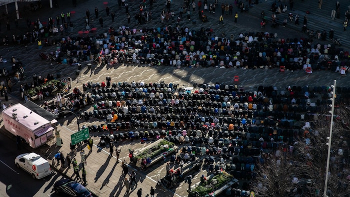 Des centaines de personnes sont rassemblées à l'extérieur et prient au sol.