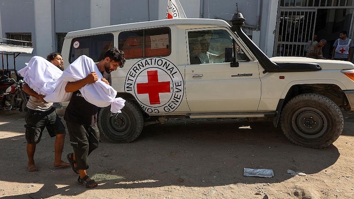 Des Palestiniens portent le corps d'une personne en passant devant un camion de la Croix-Rouge.