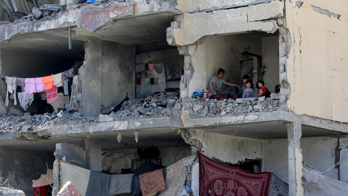 رجل فلسطيني وأطفاله يجلسون في غرفة مدمرة في مبنى سكني في مدينة رفح استهدفته غارة جوية إسرائيلية في 22 أيار (مايو) 2024.