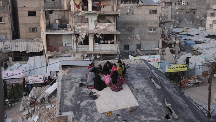 Une famille dîne sur le toit d'une maison, au milieu d'un paysage en ruines.
