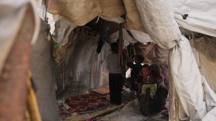 A family stand inside their damaged tent following days of rain in a makeshift camp for displaced Palestinians set up on the beach in Gaza City, Tuesday, Dec. 16, 2025. (AP Photo/Abdel Kareem Hana)