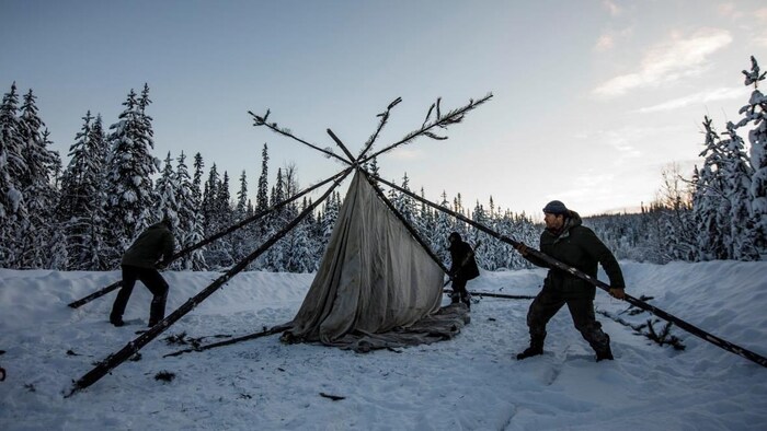 Des personnes montent une tente au milieu d'un chemin enneigé. 