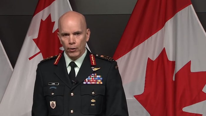 رئيس هيئة أركان الدفاع في القوات المسلحة الكندية، الجنرال واين إير، متحدثاً في مؤتمر صحفي وتبدو خلفه أعلام كندية.