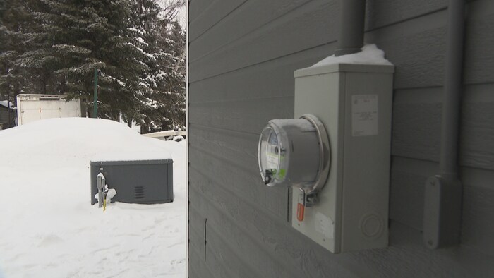 Un compteur électrique sur une maison grise, et des installations aux propanes 