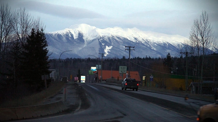 Un camion roule sur une route au pied de montagnes enneigées. 