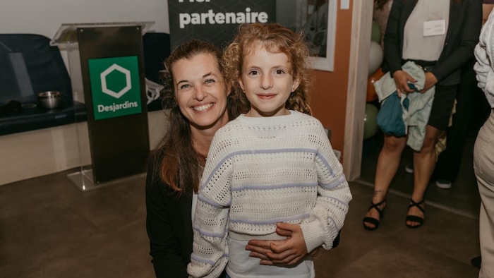 La mère et la fille posent ensemble dans un événement, la maman étant accroupie à la hauteur de sa fille.