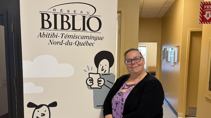 Geneviève Boucher pose devant une affiche du Réseau Biblio Abitibi-Témiscamingue Nord-du-Québec.