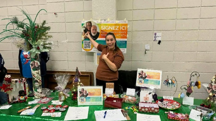 Geneviève Coutu pointe une photo d'elle et de Louis devant une table où sont disposés les documents d'une pétition.