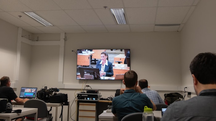 Des journalistes assis dans une salle regardent une télévision.