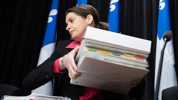 La ministre des Transports du Québec, Geneviève Guilbault, tient dans ses mains une pile de cartables lors d'un point de presse.