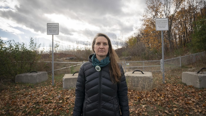 Geneviève Lussier se tient à l'extérieur de la forêt, dont l'accès est interdit au public. Une clôture et des pancartes indiquant «Propriété privée» se trouvent aux abords du terrain.