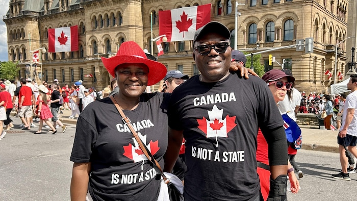 Two people with t-shirts on which it is registered in English: Canada is not a state. canada day marked "canadian pride"