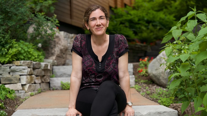 La professeure Geneviève Motard sourit à la caméra assise sur une allée de pierre.