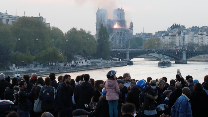Des gens regardent la fumée s'échapper de la cathédrale Notre-Dame pendant l'incendie qui s'est déclaré le 15 avril 2019. 